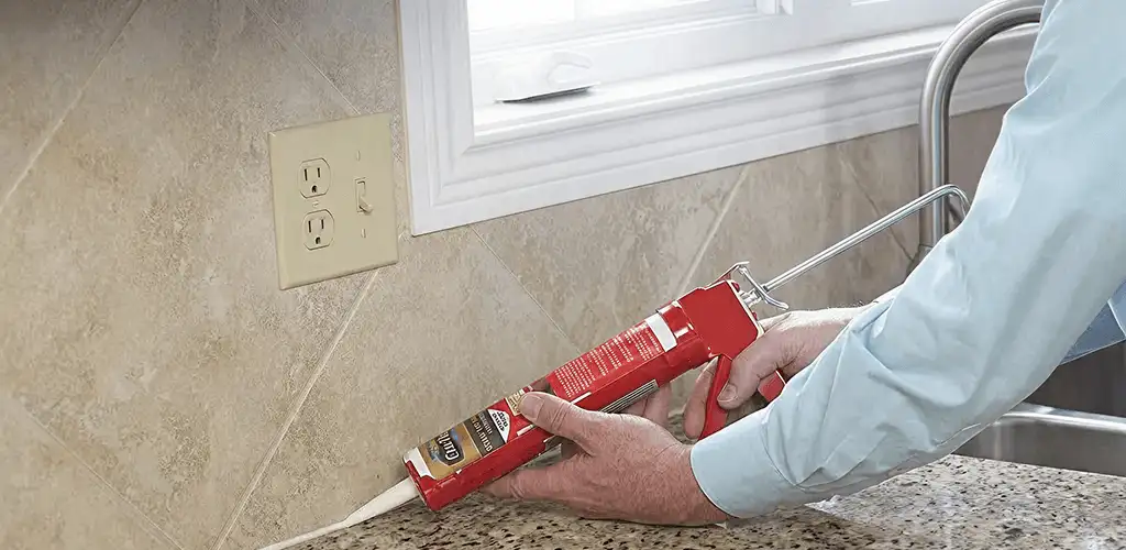 Handyman applying caulk along a kitchen backsplash and countertop seam in Albany, NY