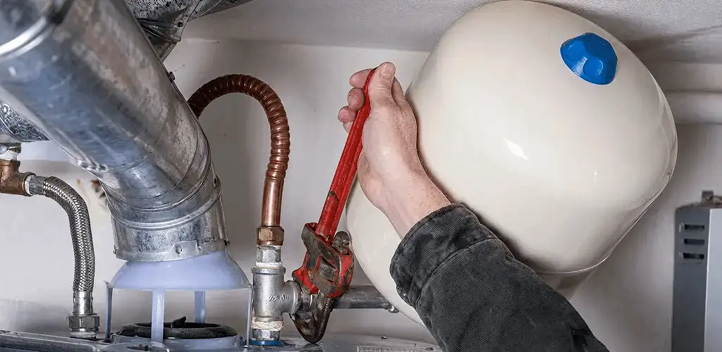 Water heater repair technician tightening plumbing connections near a tank unit in Albany, NY